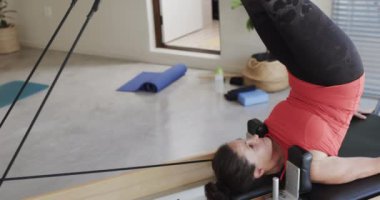 Pilates stüdyosunda değişmeden, ağır çekimde yenilikçi esneme hareketleri yapan, kıdemli, beyaz bir kadın. Egzersiz, emeklilik ve sağlıklı bir yaşam tarzı..