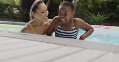 Mutlu Afro-Amerikan anne ve kızı bahçede yüzme havuzunda oynuyorlar, ağır çekimde. Yaşam tarzı, aile ve aile hayatı.