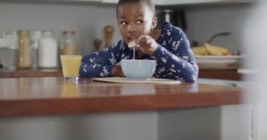 Afro-Amerikalı kız tezgahta oturuyor ve kahvaltısını mutfakta yapıyor, ağır çekimde. Yaşam tarzı, çocukluk ve ev hayatı.