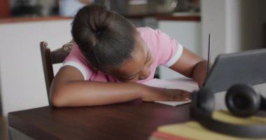 Afro-Amerikalı kız tablet kullanıyor ve ödev yapıyor, ağır çekimde. Yaşam tarzı, iletişim, öğrenme, çocukluk ve ev hayatı.