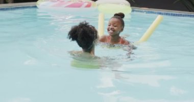 Mutlu Afro-Amerikan anne ve kızı bahçede yüzme havuzunda oynuyorlar, ağır çekimde. Yaşam tarzı, aile ve aile hayatı.