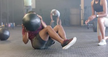 Çeşitli kadın koçlar, spor salonunda ağır çekimde tıp topuyla egzersiz yapan azimli erkekleri motive ediyor. Sağlıklı yaşam tarzı, çapraz eğitim, motivasyon, güç ve egzersiz.