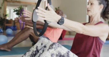 Değişik yaşlılar elinde yüzüklerle kadın pilates koçuyla ağır çekimde egzersiz yapıyor. Egzersiz, emeklilik ve sağlıklı bir yaşam tarzı..
