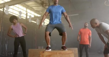 Çeşitli grup fitness sınıfı, erkek koçun boks yapmasını, spor salonunda ağır çekimde çapraz antrenman yapmasını izliyor. Sağlıklı yaşam tarzı, çapraz eğitim, fitness, motivasyon, güç ve egzersiz.