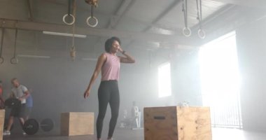 Odaklanmış Afrikalı Amerikalı kadın kutunun üstüne atlıyor, spor salonunda ağır çekimde çapraz antrenman yapıyor. Sağlıklı yaşam tarzı, çapraz eğitim, fitness, güç ve egzersiz.