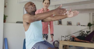 Kıdemli Afro-Amerikan erkek pilates sınıfında kadın koçla egzersiz yapıyor, değişmemiş, ağır çekimde. Egzersiz, emeklilik ve sağlıklı bir yaşam tarzı..