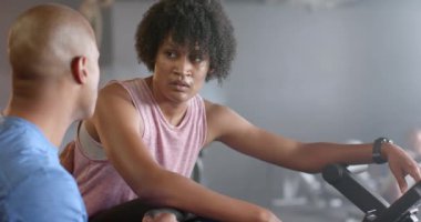 Çeşitli erkek koçlar ve eliptik bisiklete odaklanmış bir kadın spor salonunda ağır çekimde konuşuyor. Sağlıklı yaşam tarzı, çapraz eğitim, motivasyon, güç ve egzersiz.
