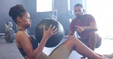 Çeşitli erkek koçlar, spor salonunda ağır çekimde tıp topuyla egzersiz yapan azimli kadınları motive ediyor. Sağlıklı yaşam tarzı, çapraz eğitim, motivasyon, güç ve egzersiz.