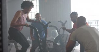 Grup fitness sınıfındaki erkekler tarafından desteklenen eliptik bisikletteki kararlı kadın, yavaş çekim. Sağlıklı yaşam tarzı, çapraz eğitim, motivasyon, güç ve egzersiz.