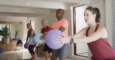 Değişik yaşlılar, kadın pilates koçuyla ağır çekimde top tutuyorlar. Egzersiz, emeklilik ve sağlıklı bir yaşam tarzı..