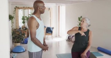 Pilates sınıfında değişmeden, ağır çekimde konuşan mutlu kıdemli erkek ve kadınlar. Egzersiz, emeklilik ve sağlıklı bir yaşam tarzı..