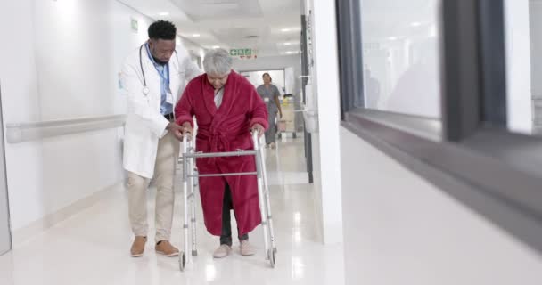 スローモーションで歩行フレームを持つ高齢者と話す幸せな多様な男性医師 変更されません 病院区 — ストック動画