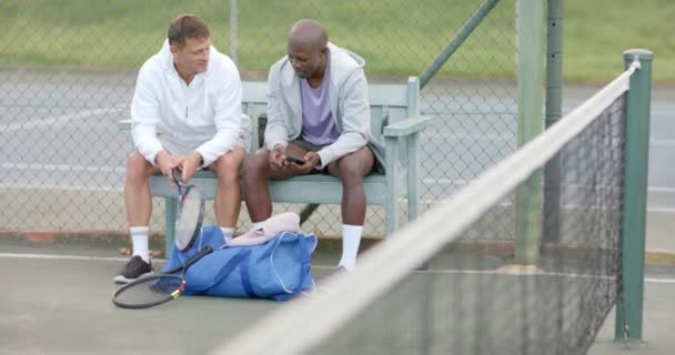 テニスコートのベンチに座っているスマートフォンを見ている幸せな多様な男性の友人 スローモーション スポーツ コミュニケーション レジャー アクティビティ — ストック動画
