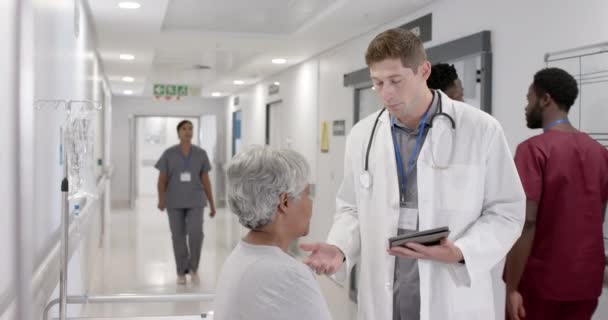 Szczęśliwy Zróżnicowany Lekarz Tabletką Rozmawiający Starszym Pacjentem Szpitalnym Łóżku Niezmieniony — Wideo stockowe