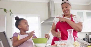 Değiştirilmemiş Afro-Amerikan anne ve kızı, mutfakta tablet kullanarak yavaş çekimde yemek pişiriyorlar. Yemek pişirme, yaşam tarzı, iletişim, aile, birliktelik ve ev hayatı.
