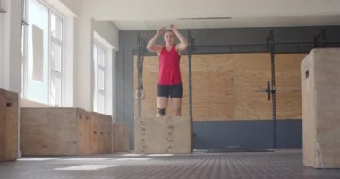 Odaklanmamış beyaz kadın kutuya atlıyor, spor salonunda çapraz antrenman yapıyor, ağır çekimde. Sağlıklı yaşam tarzı, çapraz eğitim, motivasyon, güç, fitness ve egzersiz.