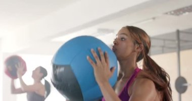Beden eğitimi sınıfında ağır çekimde tıp topu kaldıran değişmemiş melez bir kadın. Sağlıklı yaşam tarzı, çapraz eğitim, motivasyon, güç, fitness ve egzersiz.