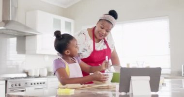 Değiştirilmemiş Afro-Amerikan anne ve kızı, mutfakta tablet kullanarak yavaş çekimde yemek pişiriyorlar. Yemek pişirme, iletişim, yaşam tarzı, aile, birliktelik ve ev hayatı.