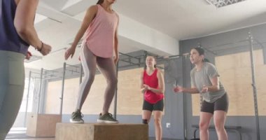 Değişmemiş farklı kadınlar azimli kadınları motive ediyor fitness sınıfında kutulara atlıyor, ağır çekimde. Sağlıklı yaşam tarzı, çapraz eğitim, motivasyon, güç, fitness ve egzersiz.