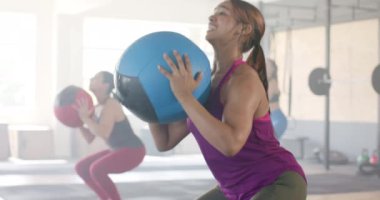 Kararlı, melez bir kadın spor salonundaki grup fitness sınıfında tıp topu kaldırıyor, ağır çekimde. Sağlıklı yaşam tarzı, çapraz eğitim, motivasyon, güç, fitness ve egzersiz.