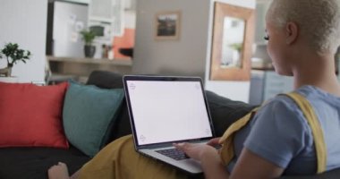 Dizüstü bilgisayarı kopyalayıp koltukta ağır çekimde oturan mutlu melez kadın. Ev hayatı, yaşam tarzı ve teknoloji.