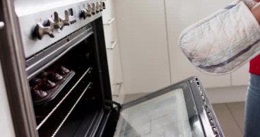 Değiştirilmemiş Afrikalı Amerikalı bir kadının mutfakta pastalarını yavaş çekimde fırından çıkarması. Aşçılık, yaşam tarzı ve ev hayatı.