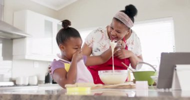 Değiştirilmemiş Afro-Amerikan anne ve kızı, mutfakta tablet kullanarak yavaş çekimde yemek pişiriyorlar. Yemek pişirme, iletişim, yaşam tarzı, aile, birliktelik ve ev hayatı.