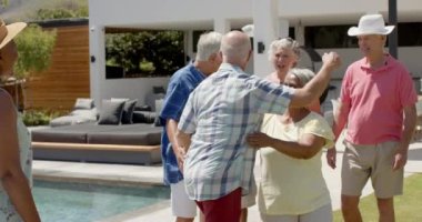 Mutlu kıdemli arkadaşlar güneşli bahçe partisinde yavaş çekimde konuşuyorlar ve kucaklaşıyorlar. Arkadaşlık, yaz, kıdemli yaşam tarzı, birliktelik ve kutlama..