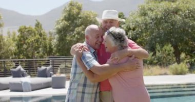 Güneşli bahçe partisinde değişmeden ağır çekimde kucaklaşan mutlu kıdemli arkadaşların portresi. Arkadaşlık, yaz, kıdemli yaşam tarzı, birliktelik ve kutlama..