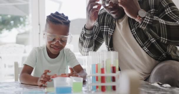 アフリカ系アメリカ人の父親と息子は ゆっくりとした動きで 液体で試験管を保持してテーブルに座っています 家庭生活 — ストック動画