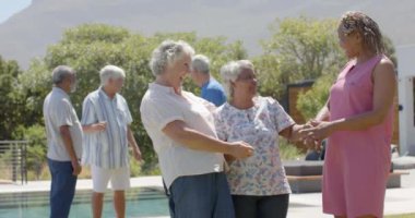 Güneşli bahçe partisinde değişmeden, ağır çekimde kucaklaşan mutlu kıdemli bayan arkadaşlar. Arkadaşlık, yaz, kıdemli yaşam tarzı, birliktelik ve emeklilik.