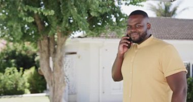 Mutlu Afro-Amerikan bir adamın portresi bahçede akıllı telefondan konuşuyor, fotokopi odası, ağır çekim. Yaşam tarzı, iletişim ve ev hayatı.