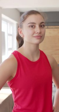 Spor salonunda yavaş çekimde gülümseyen mutlu, değişmemiş beyaz kadının dikey video portresi. Sağlıklı yaşam tarzı, çapraz eğitim, motivasyon, güç ve egzersiz.