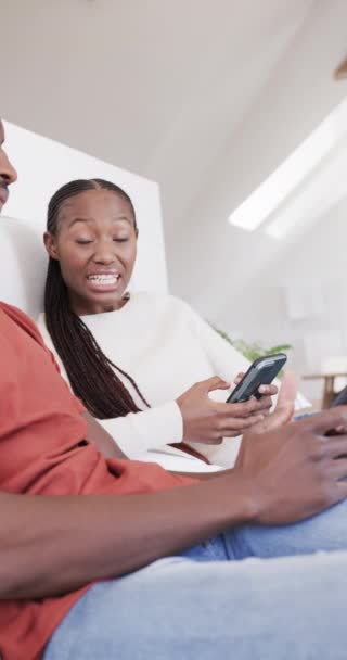 スローモーションで自宅でスマートフォンを使用して幸せなアフリカ系アメリカ人夫婦の垂直ビデオ 家庭生活 ライフスタイル — ストック動画