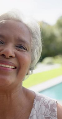 Bahçedeki kameraya bakan son sınıf mutlu çift ırklı kadının dikey videosu, yavaş çekim. Kıdemli yaşam tarzı, boş zaman, yaz ve doğa, değişmemiş..