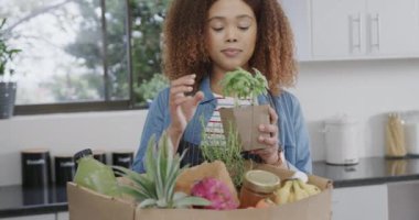 Melez kadının alışveriş paketlerini açması ve mutfakta ot koklaması, ağır çekimde. Yiyecek, alışveriş, sağlıklı yaşam ve ev hayatı, değişmemiş..
