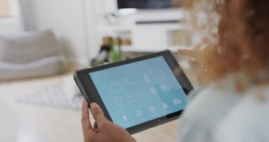 Evde akıllı arayüzü olan tablet kullanan melez bir kadın oturma odasında, ağır çekimde. Teknoloji, iletişim, kontrol, yaşam tarzı ve ev hayatı, değiştirilmemiş.