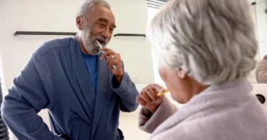 Banyoda dişlerini fırçalayan, değiştirilmemiş, ağır çekimde mutlu çift. Kıdemli yaşam tarzı, kişisel bakım ve ev hayatı..