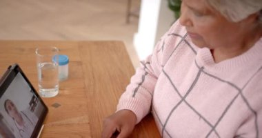 Melez bir kadın melez doktor ile tıbbi danışmanlık için tablet kullanıyor. Ağır çekimde. Kıdemli yaşam tarzı, sağlık hizmeti, tıbbi danışmanlık, iletişim ve ev hayatı, değişmemiş.