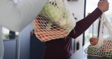 Çift ırklı lezbiyen çiftin orta kesimi alışveriş torbalarını yavaş çekimde mutfağa boşaltıyor. İlişki, alışveriş, yemek, sağlıklı yaşam tarzı, birliktelik ve aile hayatı, değişmemiş..