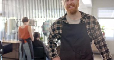 Kuaförde gülümseyen önlüklü beyaz erkek kuaför portresi, fotokopi odası, ağır çekim. Yerel iş, iş, iş sahibi, kuaför, saç bakımı ve kuaförlük, değişmemiş.