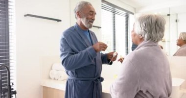 Banyoda dişlerini fırçalayan, değiştirilmemiş, ağır çekimde mutlu çift. Kıdemli yaşam tarzı, kişisel bakım ve ev hayatı..