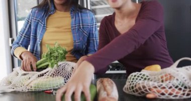 Çift ırklı lezbiyen çiftin orta kesimi alışveriş torbalarını yavaş çekimde mutfağa boşaltıyor. İlişki, alışveriş, yemek, sağlıklı yaşam tarzı, birliktelik ve aile hayatı, değişmemiş..