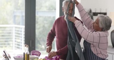 Üst düzey melez çift önlük giyip mutfakta sebze doğruyor. Değiştirilmemiş, ağır çekimde. Kıdemli yaşam tarzı, aşçılık ve ev hayatı..