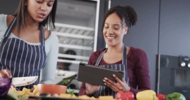 Önlüklü, yemek hazırlayan ve mutfakta tablet kullanan mutlu çift. Yavaş çekimde. Aşçılık, yemek, sağlıklı yaşam tarzı, birliktelik, iletişim, tarif ve ev hayatı, değişmemiş.