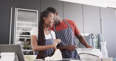 Afro-Amerikan önlüklü mutlu çift mutfakta tablet kullanarak yemek pişiriyorlar, ağır çekimde. Yaşam tarzı, yemek pişirme, ekmek, birliktelik, yemek ve ev hayatı, değişmemiş.