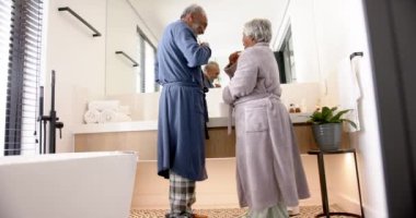 Banyoda dişlerini fırçalayan, değiştirilmemiş, ağır çekimde mutlu çift. Kıdemli yaşam tarzı, kişisel bakım ve ev hayatı..