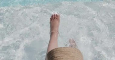 Güneş şapkalı melez bir kadın havuzda ağır çekimde oturuyor. Yaz, güneşli, hafta sonu, boş zaman, yaşam tarzı ve tatil.