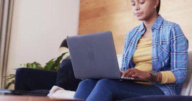 Oturma odasında dizüstü bilgisayarı yavaş çekimde kullanan çift ırklı bir kadın. Yaşam tarzı, uzaktan çalışma, iletişim, evden çalışma, teknoloji ve ev yaşamında değişiklik yok..