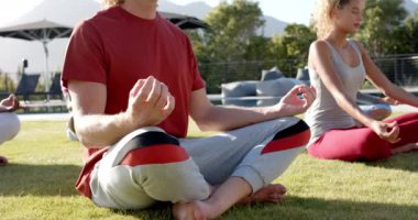 Yoga yapan farklı arkadaşlar güneşli bahçede yavaş çekimde birlikte oturuyorlar. Sağlıklı yaşam tarzı, rahatlama, nilüfer pozisyonu, arkadaşlık ve refah, değişmemiş..